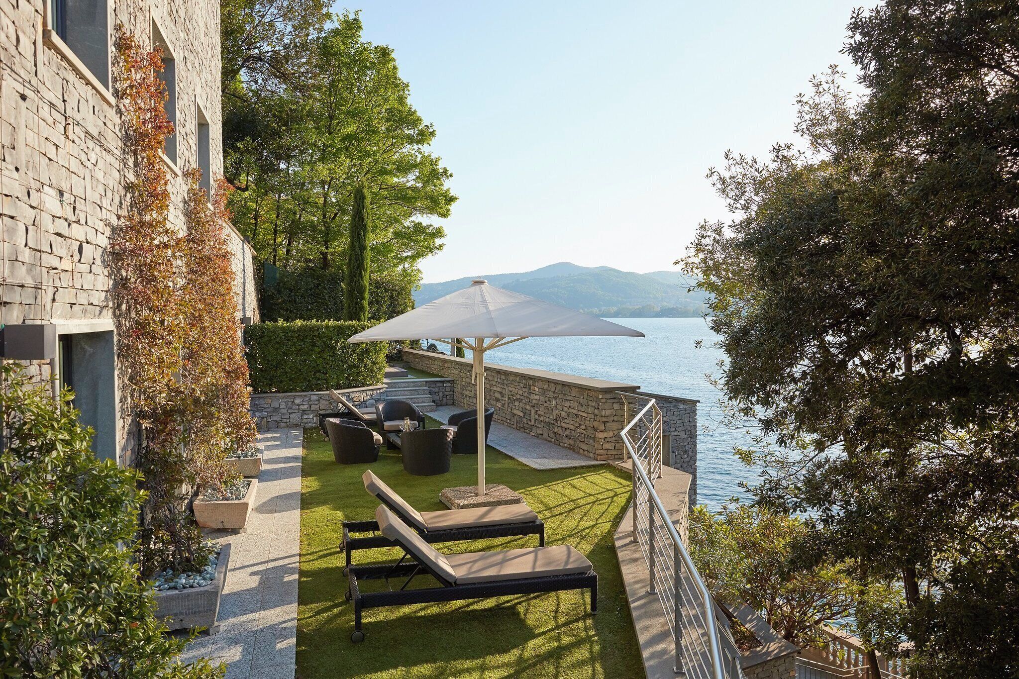 Una terrazza con poltrone da relax e un tavolo, con vista su uno specchio d'acqua e montagne.