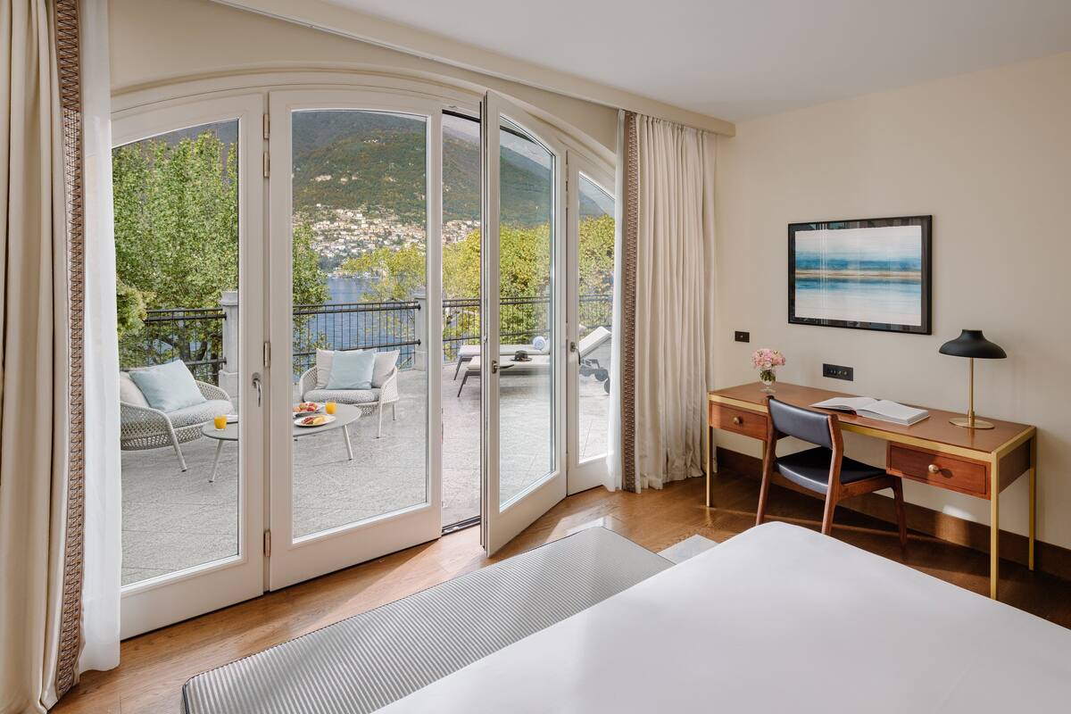 Una habitación de hotel con una cama, un escritorio y vistas a un balcón con mobiliario exterior.