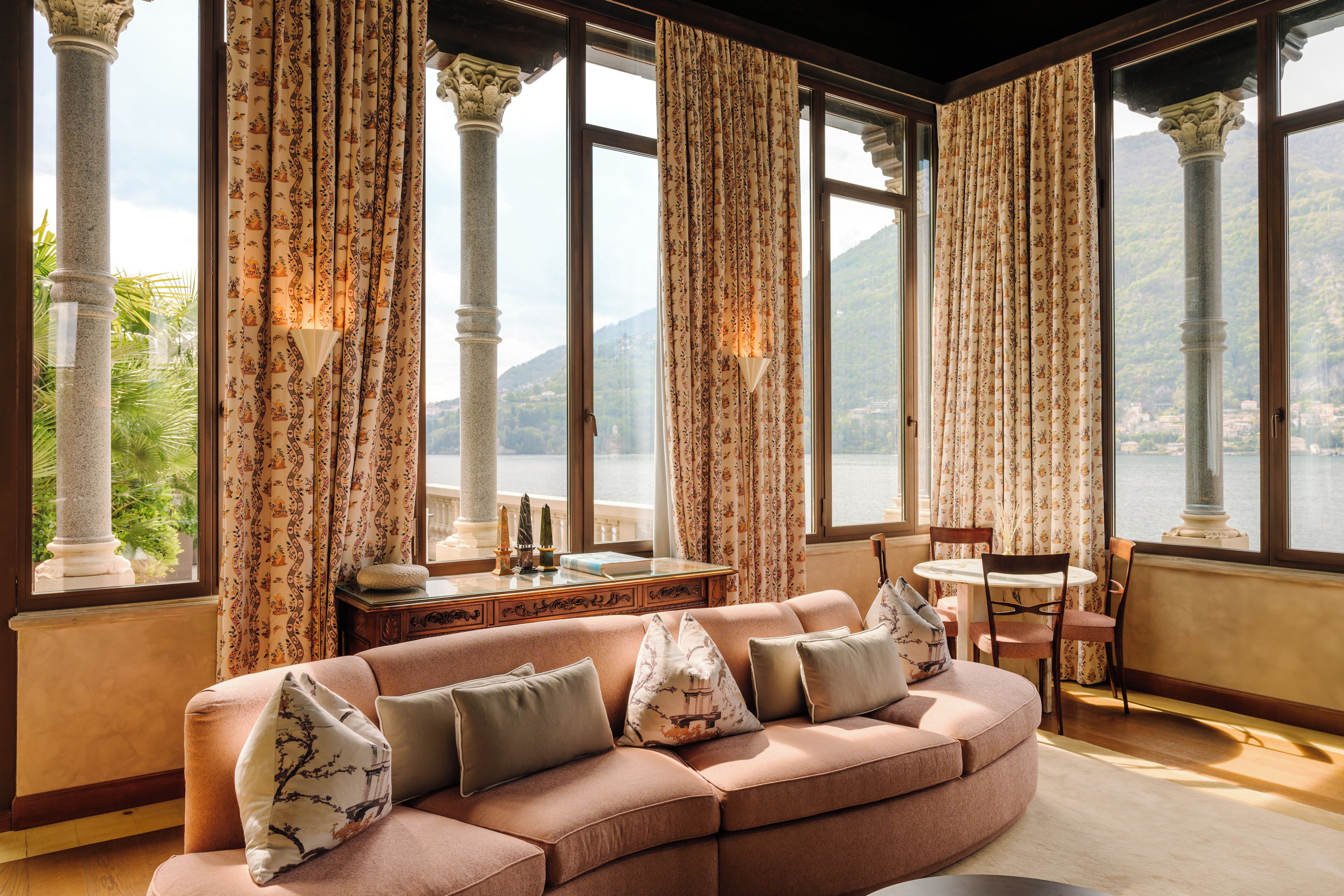 A room with a sofa, a table, and a view of a lake through large windows.