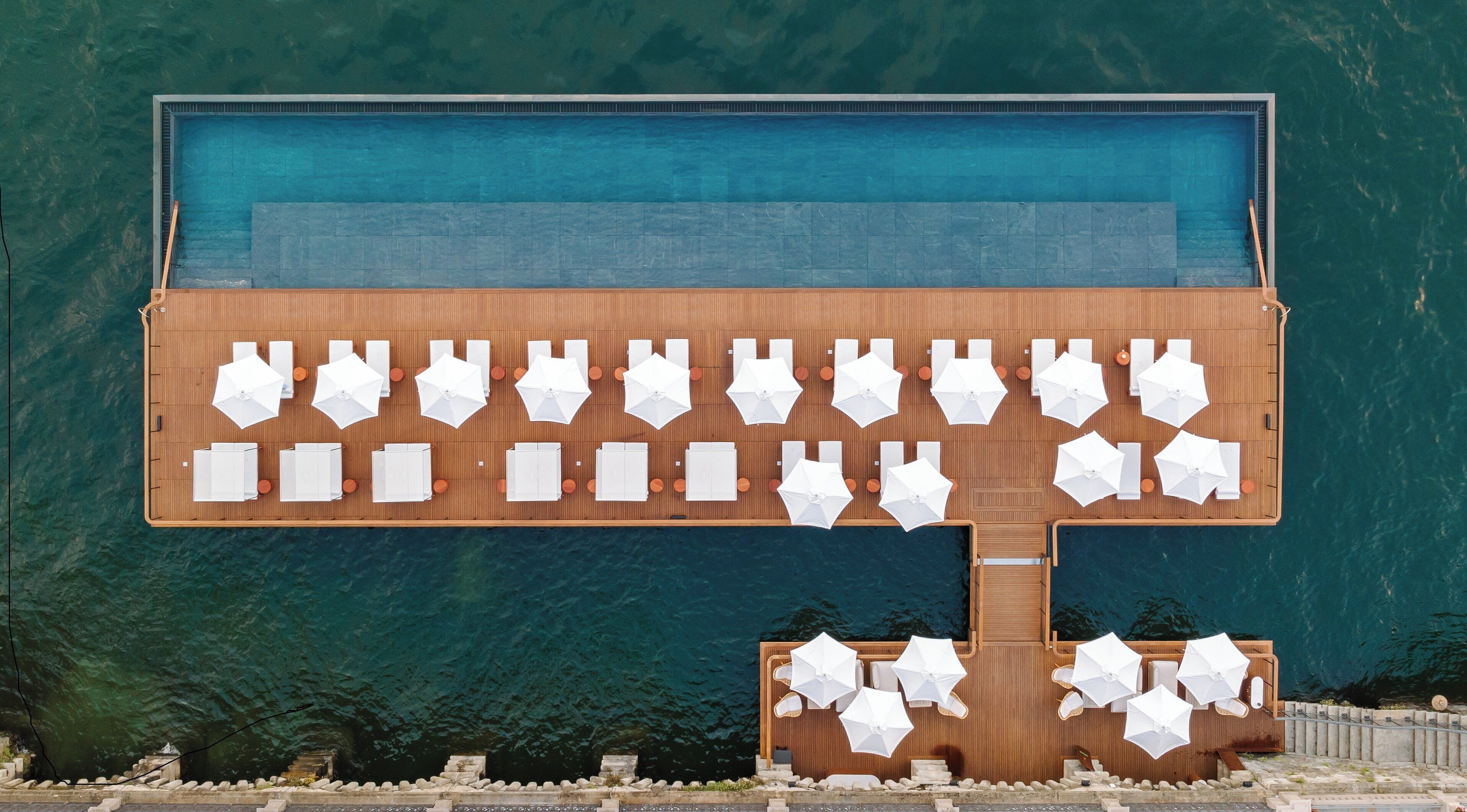 Une grande piscine entourée d’une terrasse en bois, agrémentée de plusieurs chaises longues et de parasols.