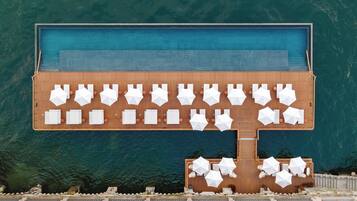 Une grande piscine entourée d’une terrasse en bois, agrémentée de plusieurs chaises longues et de parasols.