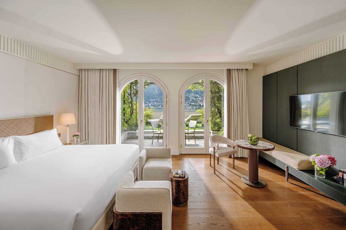 Habitación de hotel con una cama grande, televisor, zona de estar con mesa y vistas al exterior.