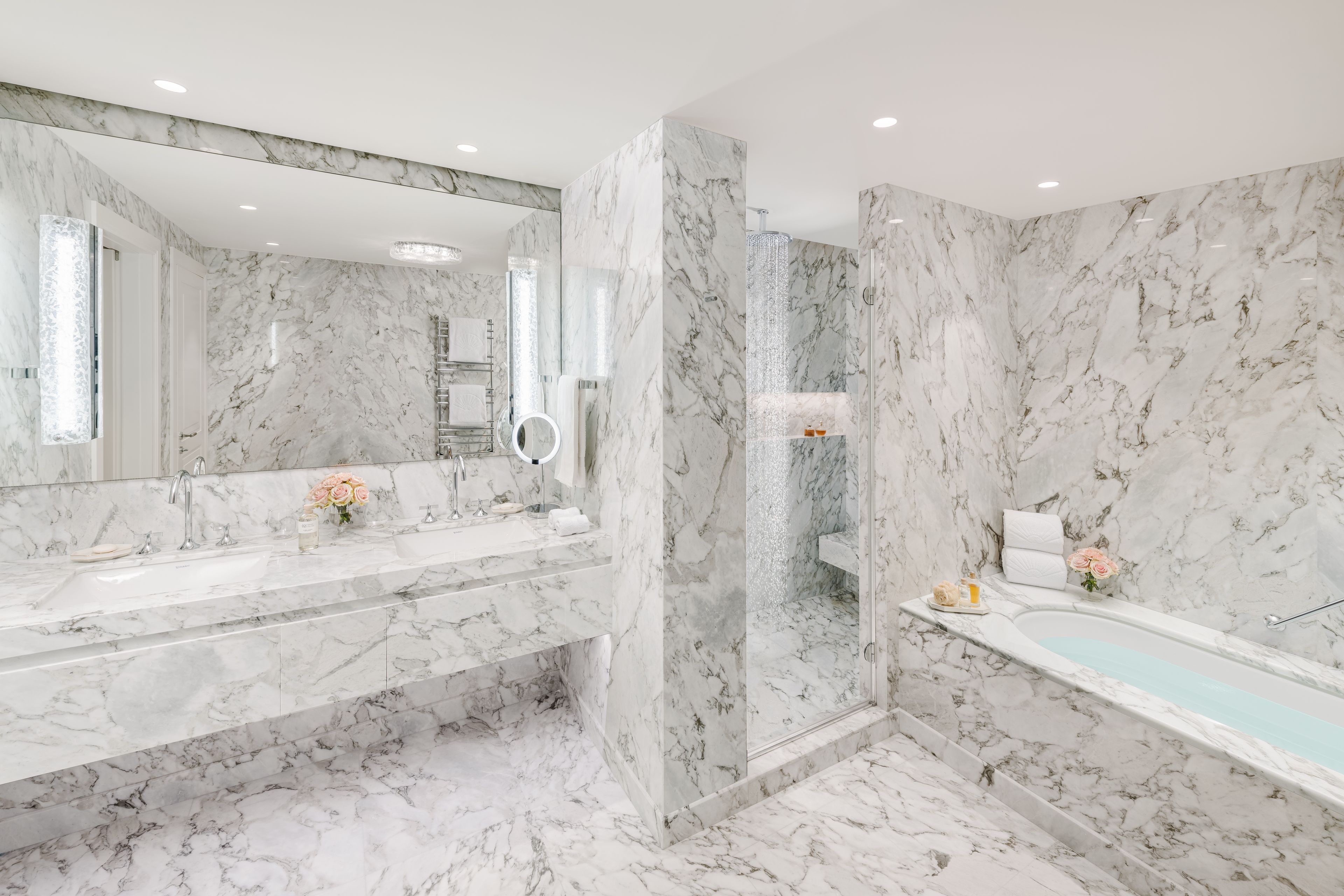 Un baño con paredes de mármol, una bañera, una ducha y un tocador con espejo.
