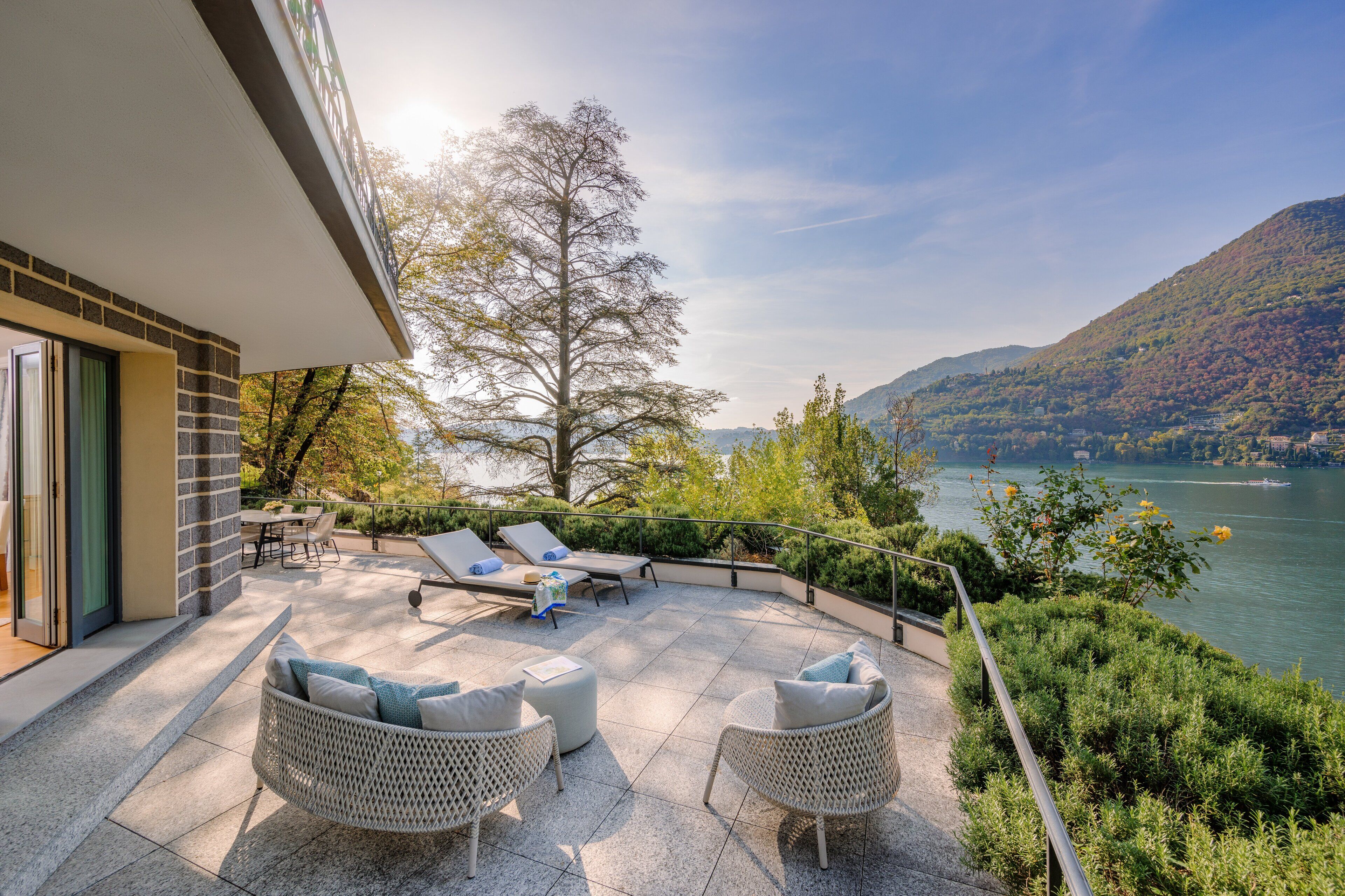 Una terraza con asientos al aire libre, vista a un lago y follaje circundante.