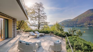 Una terraza con asientos al aire libre, vista a un lago y follaje circundante.