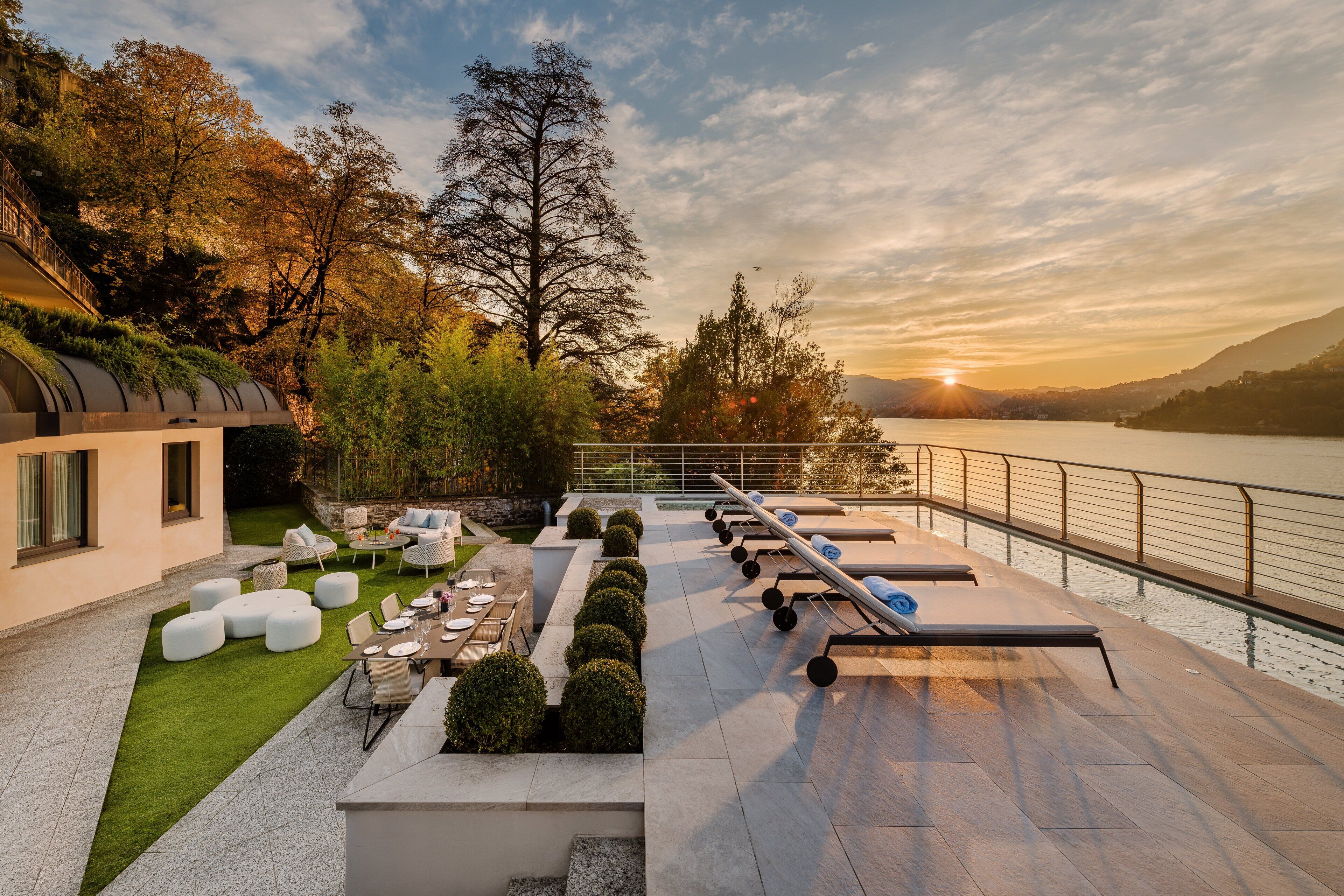 A modern outdoor patio with seating, a pool, and a view of the lake at sunset.