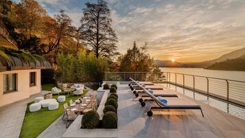 A modern outdoor patio with seating, a pool, and a view of the lake at sunset.