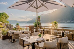 An outdoor dining area with tables and chairs, overlooking a lake and mountains. - Mandarin Oriental, Lago di Como (Blevio)