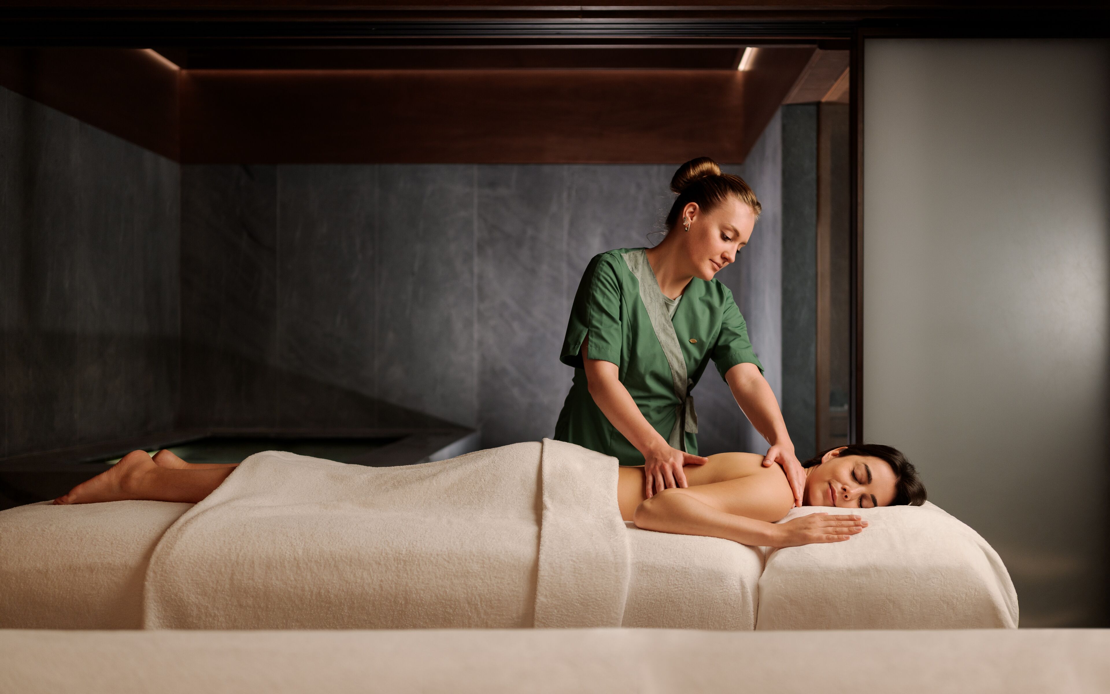 Una sesión de masoterapia en un spa, con una sala de tonos oscuros y una camilla de masaje.