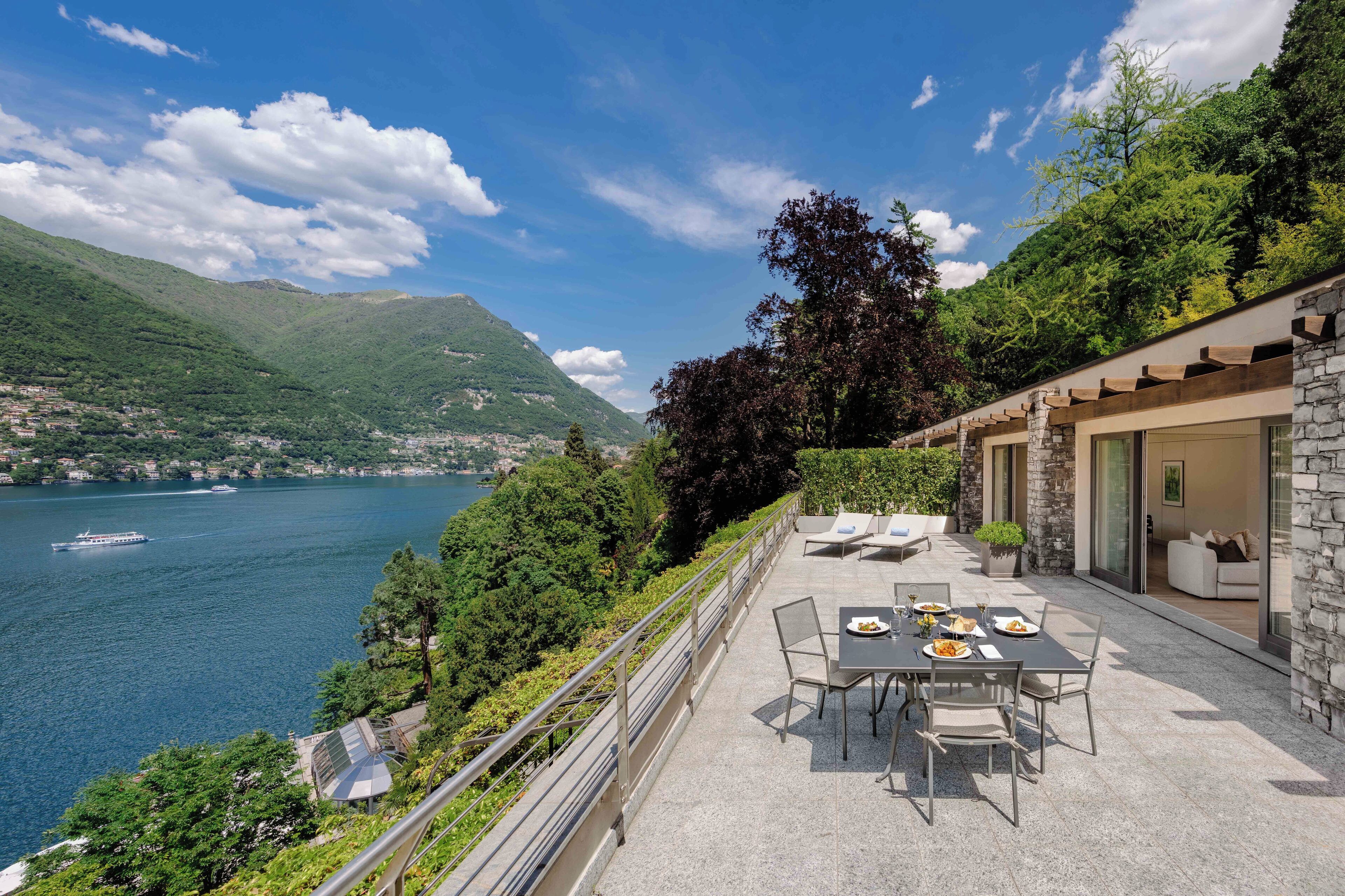 A terrace with a table set for dining, overlooking a lake and mountains.