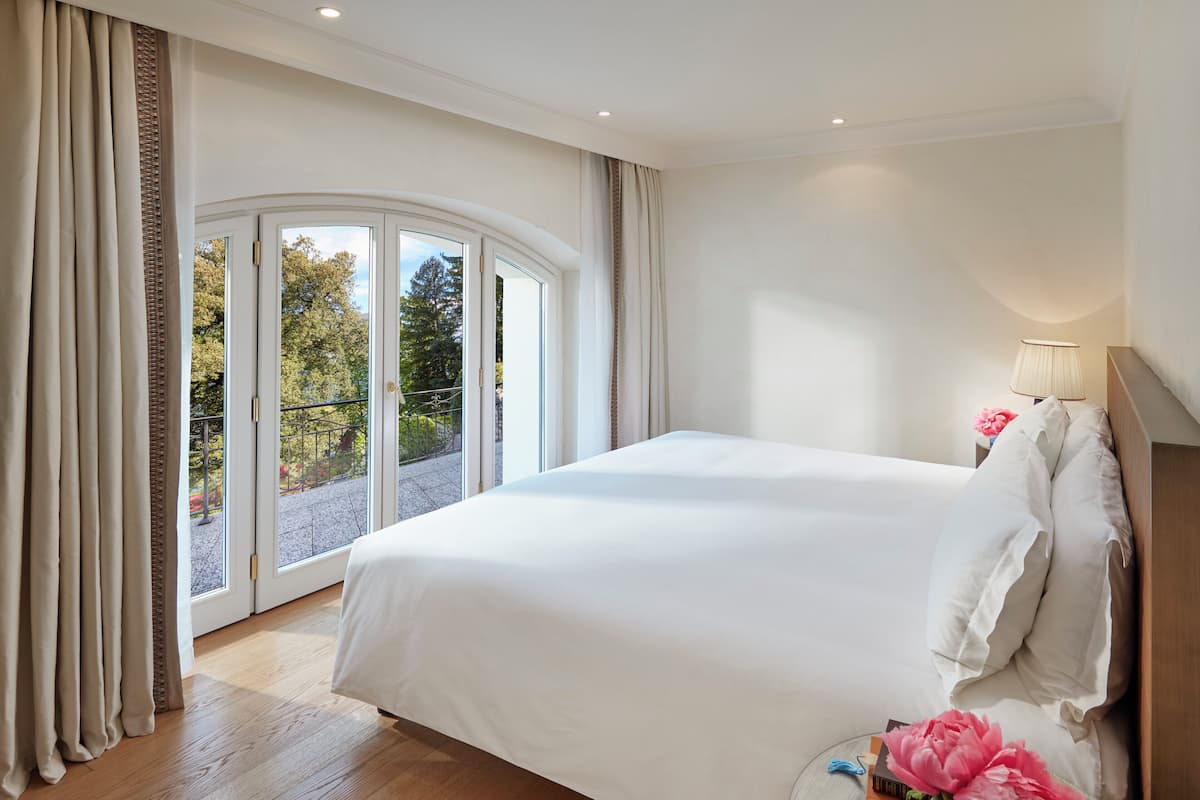 Una cama grande en una habitación de hotel con vistas a árboles a través de puertas de cristal.