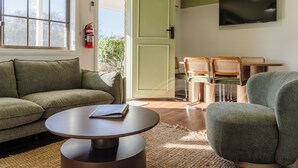 Una habitación con sofá, una mesa redonda, dos sillas, televisor y una puerta que da al exterior.