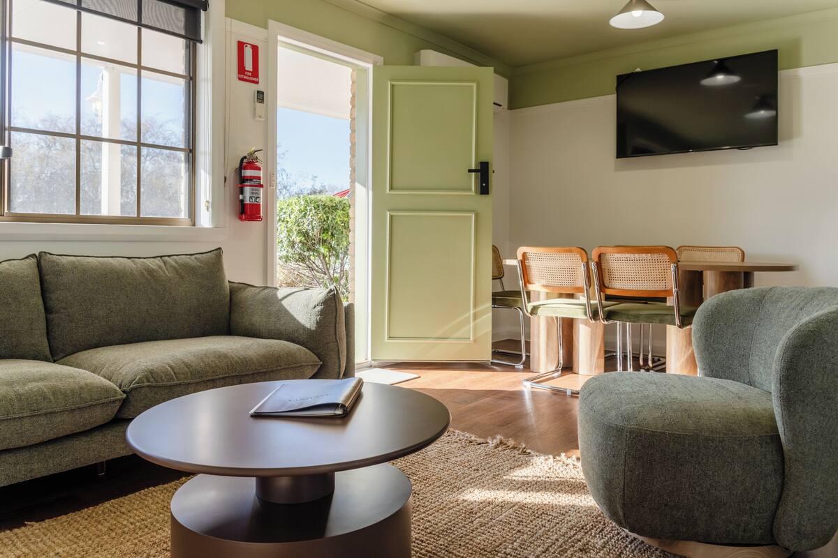 A room with a sofa, a round table, two chairs, a television, and a door leading outside.