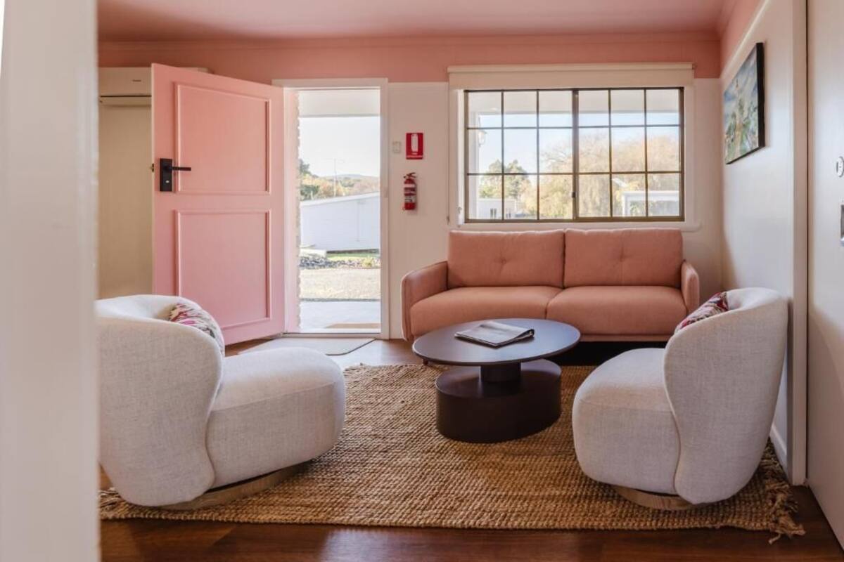 A room with a pink door, a sofa, two armchairs, a coffee table, and a window with a view.