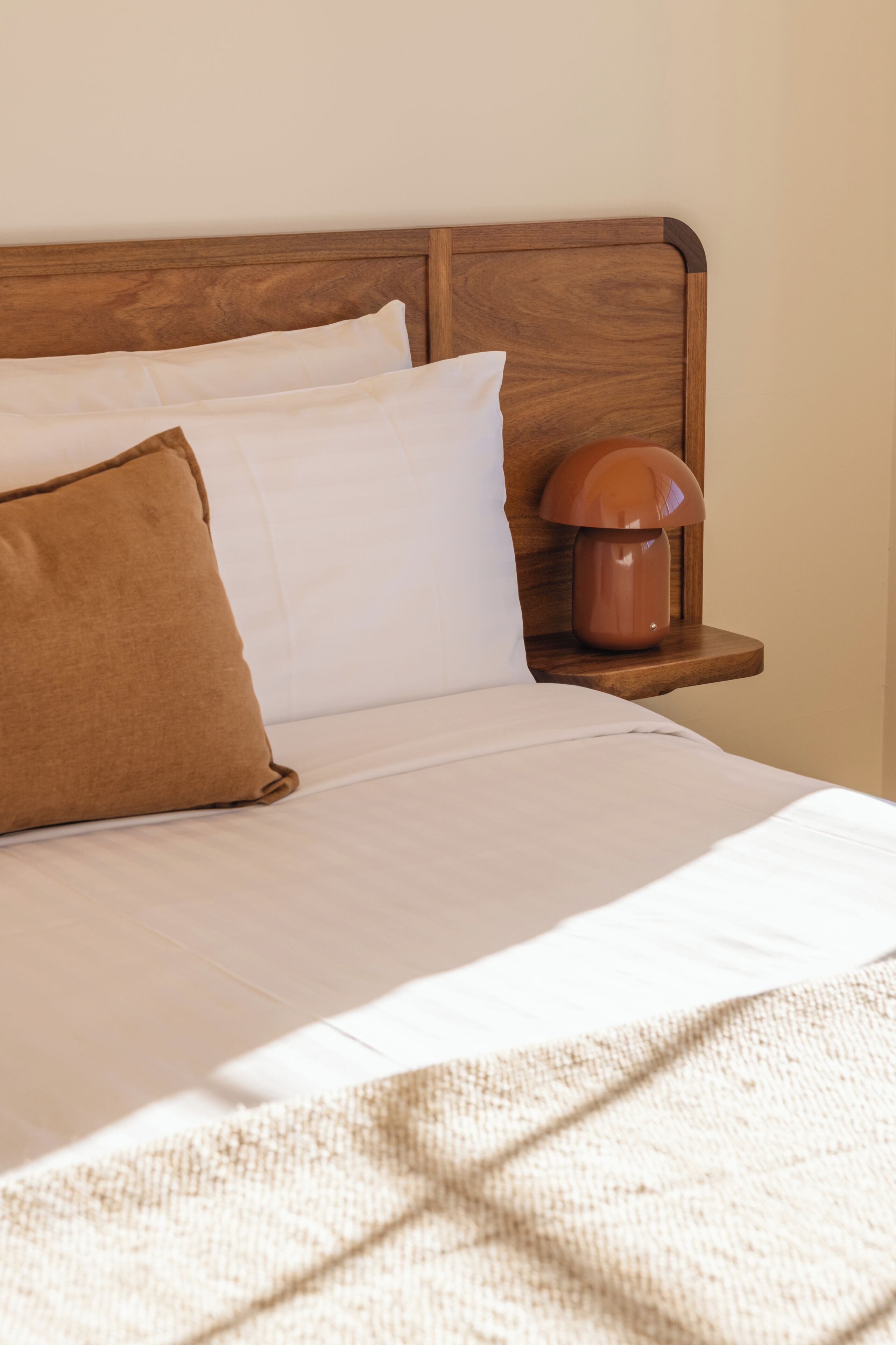 Una cama bien hecha con cabecera de madera, almohada marrón y lámpara de noche.