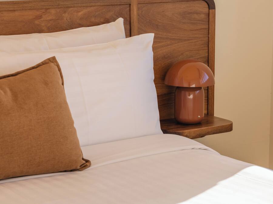 Una cama bien hecha con cabecera de madera, almohada marrón y lámpara de noche.