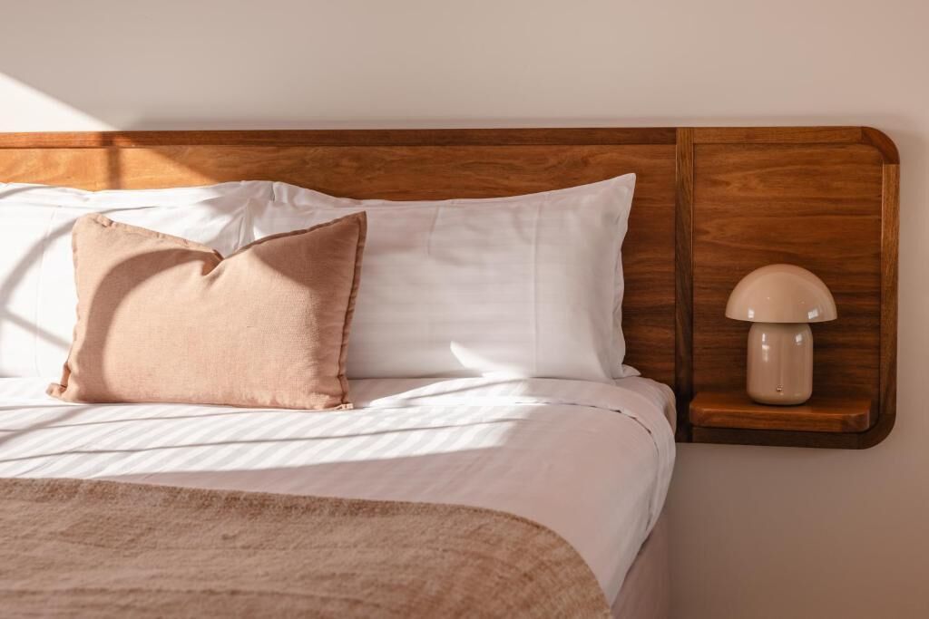 A neatly made bed with a wooden headboard, a bedside lamp, and a single decorative pillow.