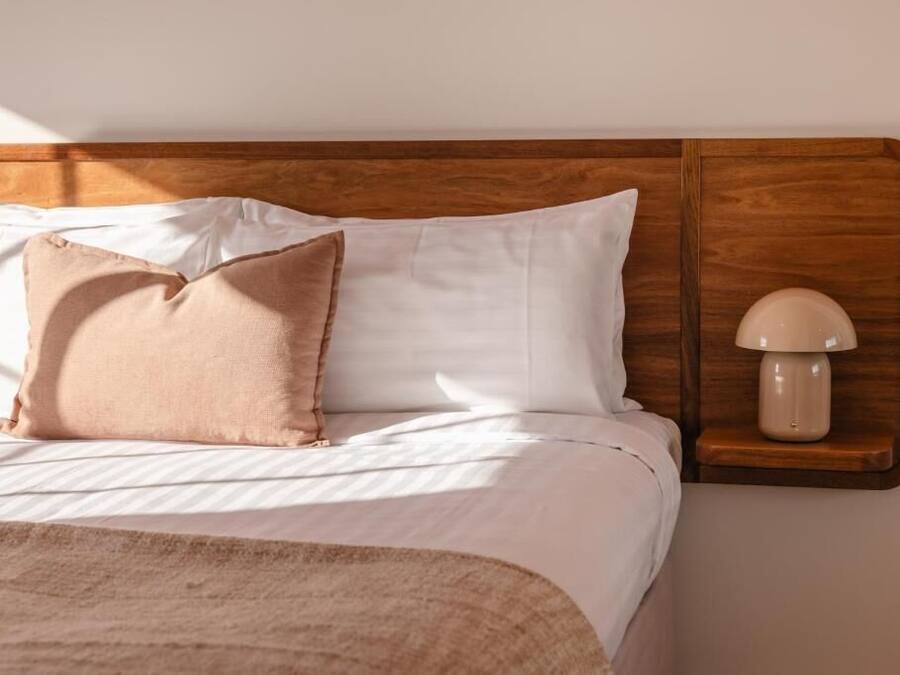 A neatly made bed with a wooden headboard, a bedside lamp, and a single decorative pillow.