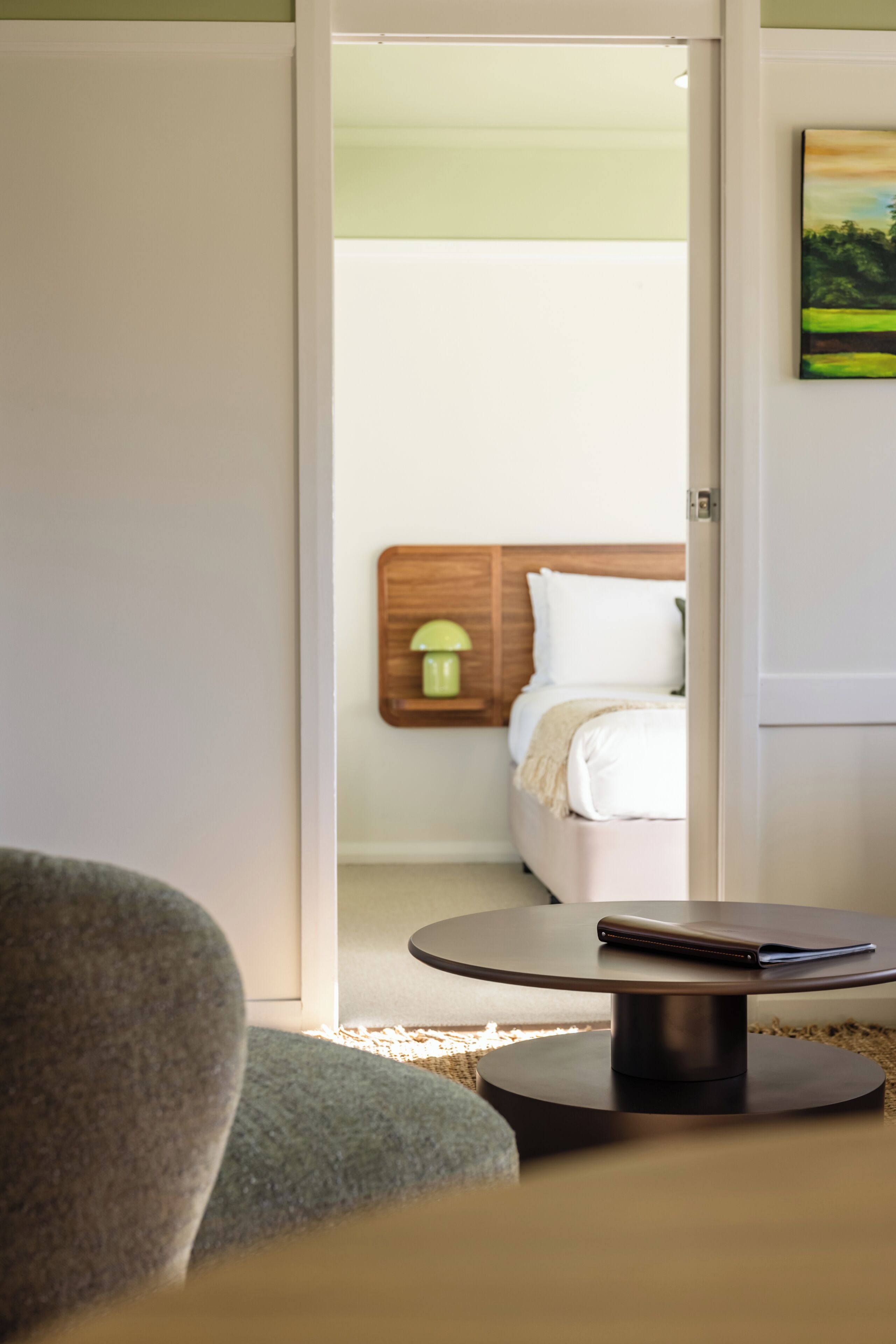 A hotel room with a bed, a bedside table, a lamp, and a painting on the wall.
