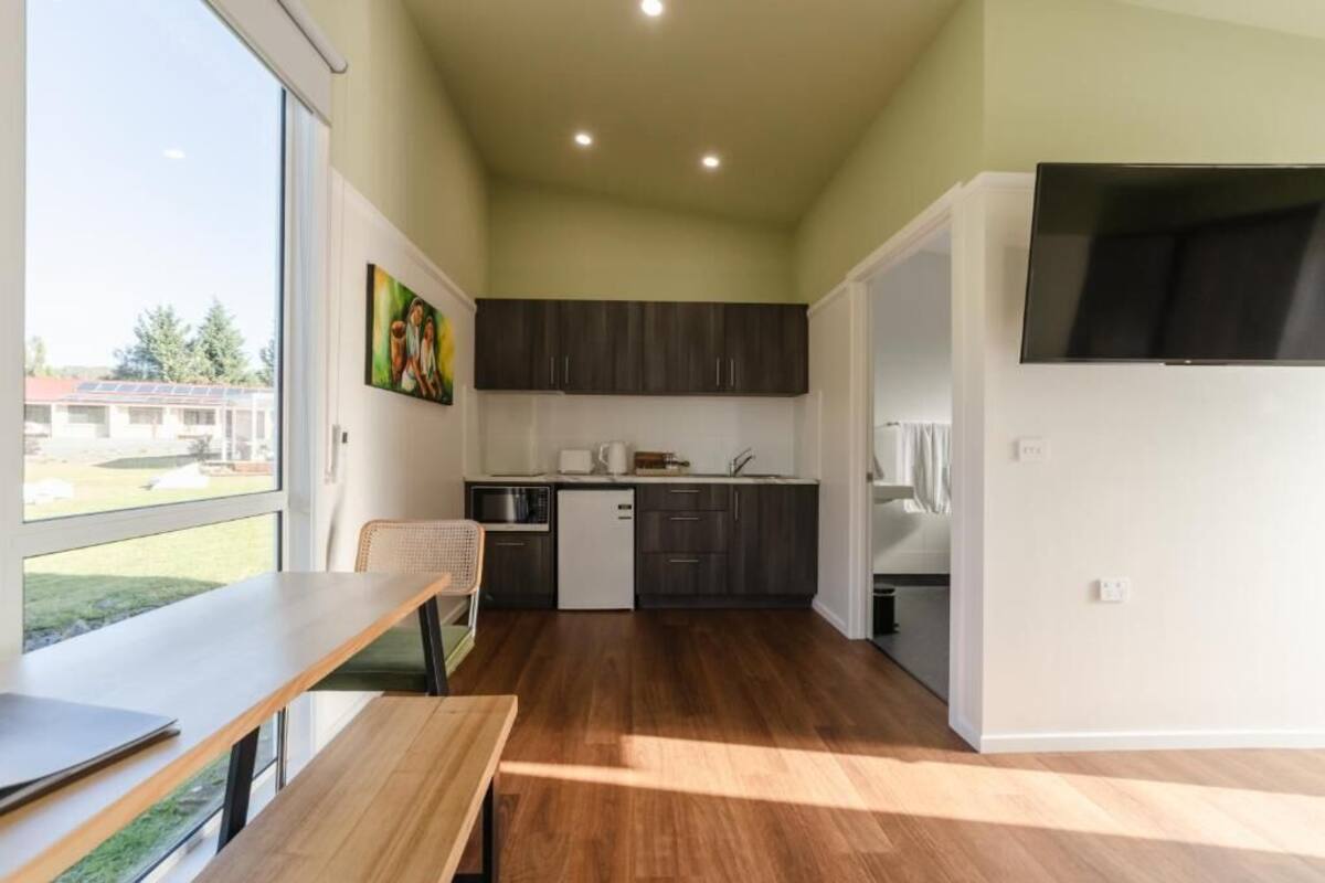 A modern kitchen with dark cabinets, a dining area with a table and chairs, and a large window providing a view of the outdoors.