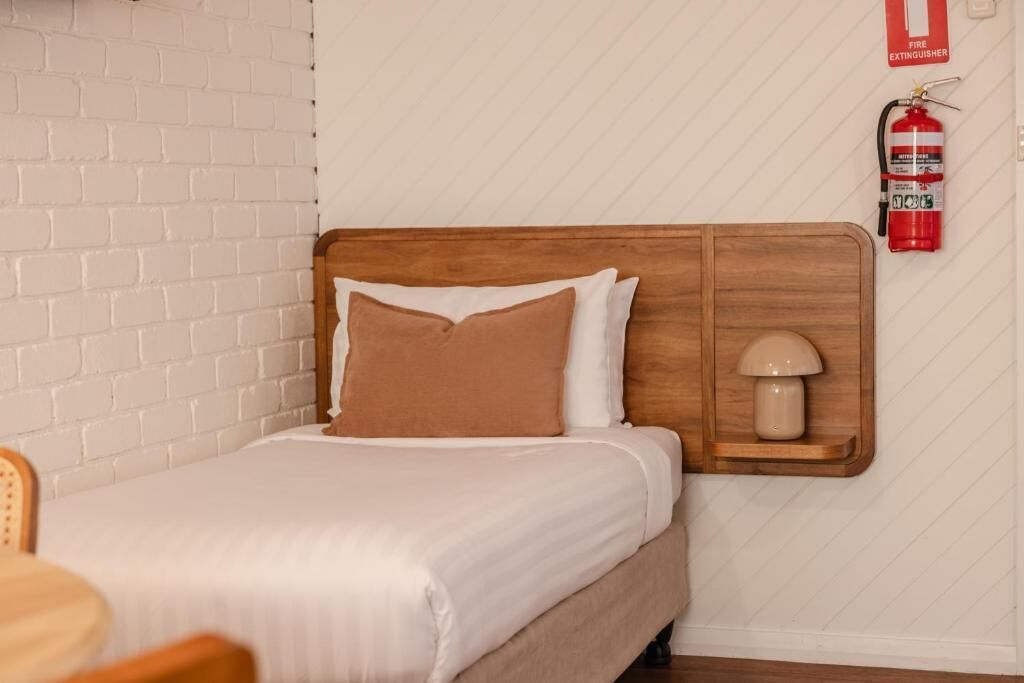 A bed with a wooden headboard, a bedside lamp, and a fire extinguisher on the wall.