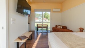 A bedroom with a bed, a TV mounted on the wall, a bench, and a view of the outside. - Amadiya Port Arthur Villas (Port Arthur)