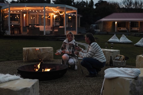 An outdoor seating area with a fire pit, stone seating, and a covered structure with string lights.