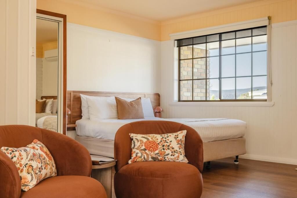 A bedroom with a bed, two chairs, a small table, and a window with a view.