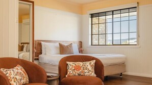 Un dormitorio con cama, dos sillas, una mesita y ventana con vistas.