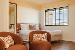 Quarto com cama, duas cadeiras, uma mesinha e janela com vista.