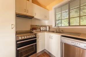 A kitchen with white cabinets, a stainless steel oven, a dishwasher, and a window with blinds. - Amadiya Port Arthur Villas (Port Arthur)