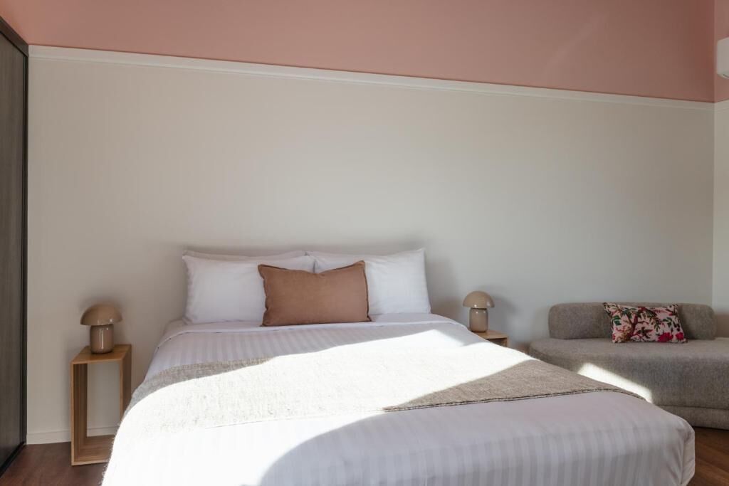 A bedroom with a bed, bedside tables, a sofa, and a wall with a window.