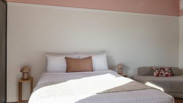 A bedroom with a bed, bedside tables, a sofa, and a wall with a window.