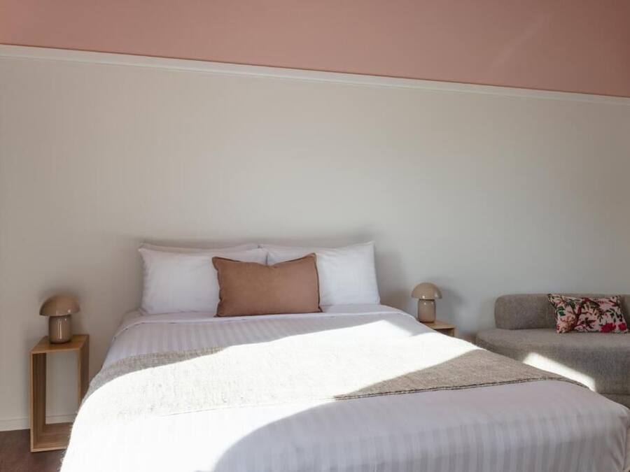 A bedroom with a bed, bedside tables, a sofa, and a wall with a window.
