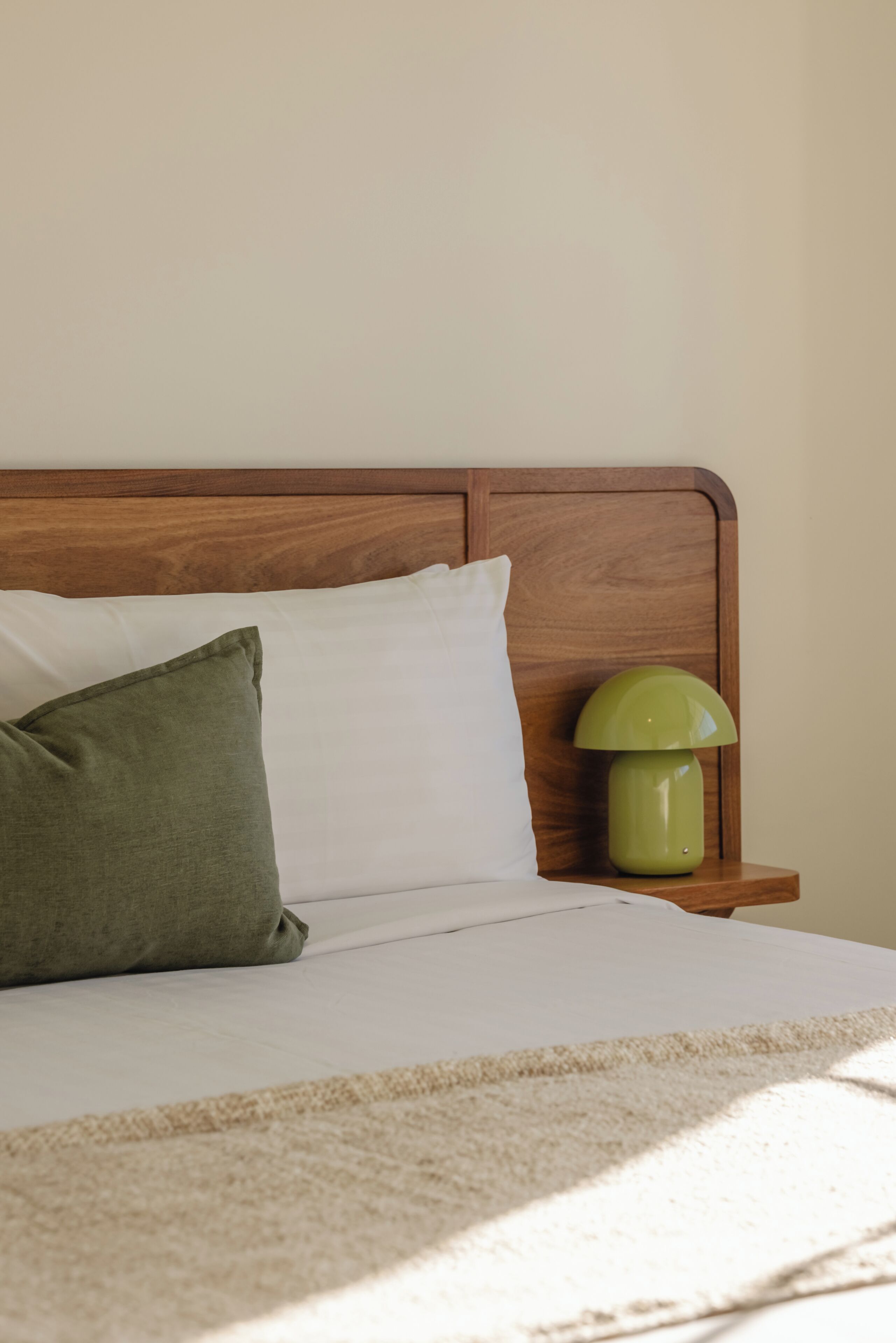 A bed with a wooden headboard, a green pillow, a white pillow, and a green lamp on a bedside table.
