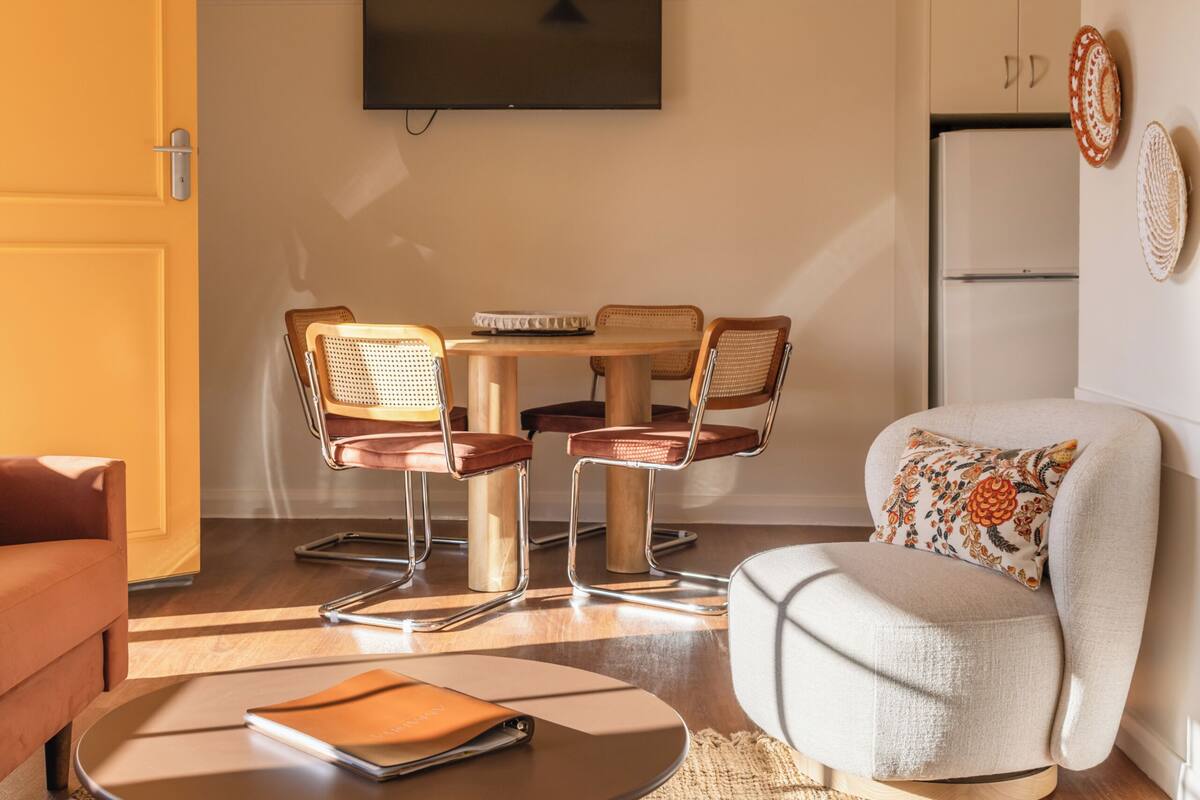 A modern living room with a round coffee table, a sofa, a dining table with chairs, and a flat-screen TV mounted on the wall.