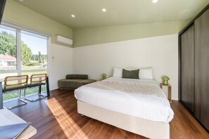 A bedroom with a bed, a bench, and a view of a green outdoor area. - Amadiya Port Arthur Villas (Port Arthur)