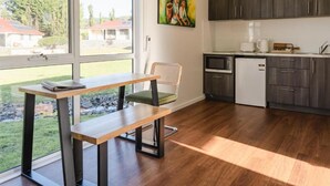 A modern kitchen with dark cabinets, a microwave, and a refrigerator. There is a dining area with a table and chairs, and a painting on the wall. - Amadiya Port Arthur Villas (Port Arthur)
