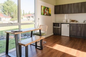 A modern kitchen with dark cabinets, a microwave, and a refrigerator. There is a dining area with a table and chairs, and a painting on the wall. - Amadiya Port Arthur Villas (Port Arthur)