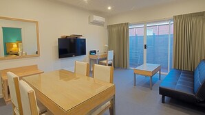 A hotel room with a wooden dining table, a sofa, a TV, and a sliding glass door to the outside. - Brighton Serviced Apartments (Brighton)