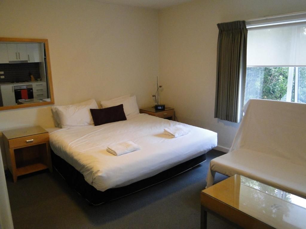 A hotel room with a bed, bedside table, chair, and a window with curtains.
