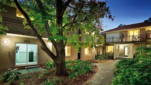 A building with a reception area, a tree-lined pathway, and a balcony with outdoor seating. - Brighton Serviced Apartments (Brighton)