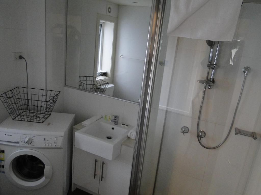 A compact bathroom with a washing machine, a sink, and a shower enclosure.