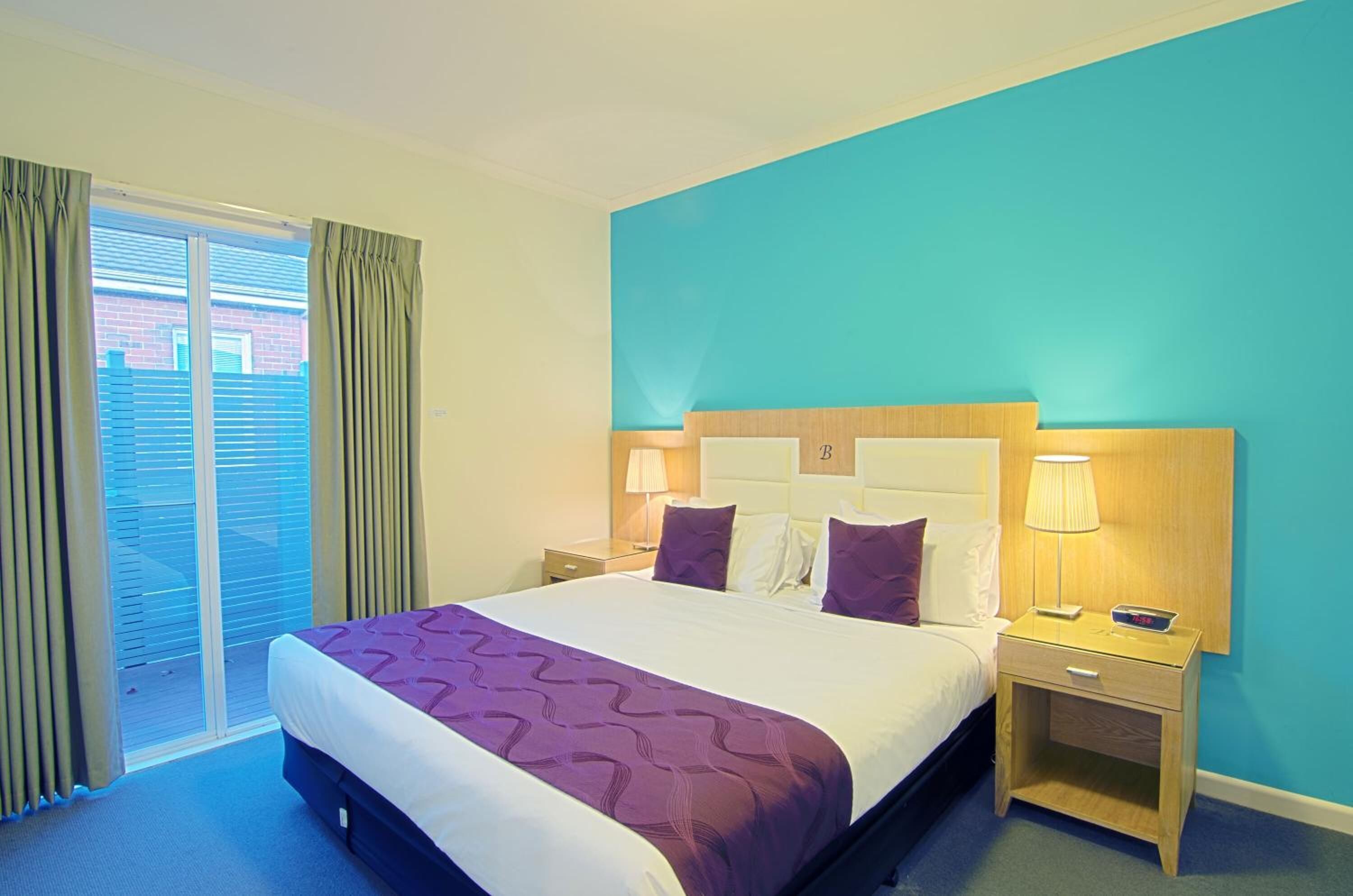 Habitación de hotel con una cama grande, dos mesitas de noche, una ventana con cortinas y vistas a un edificio.