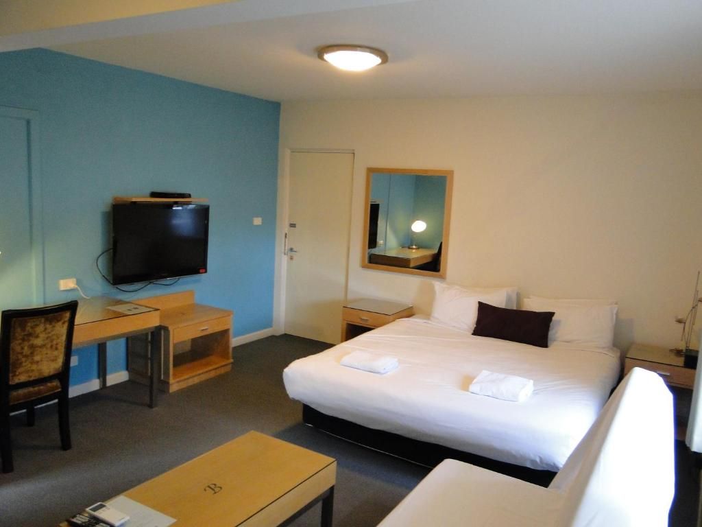 A hotel room with a bed, a desk, a television, and a mirror.