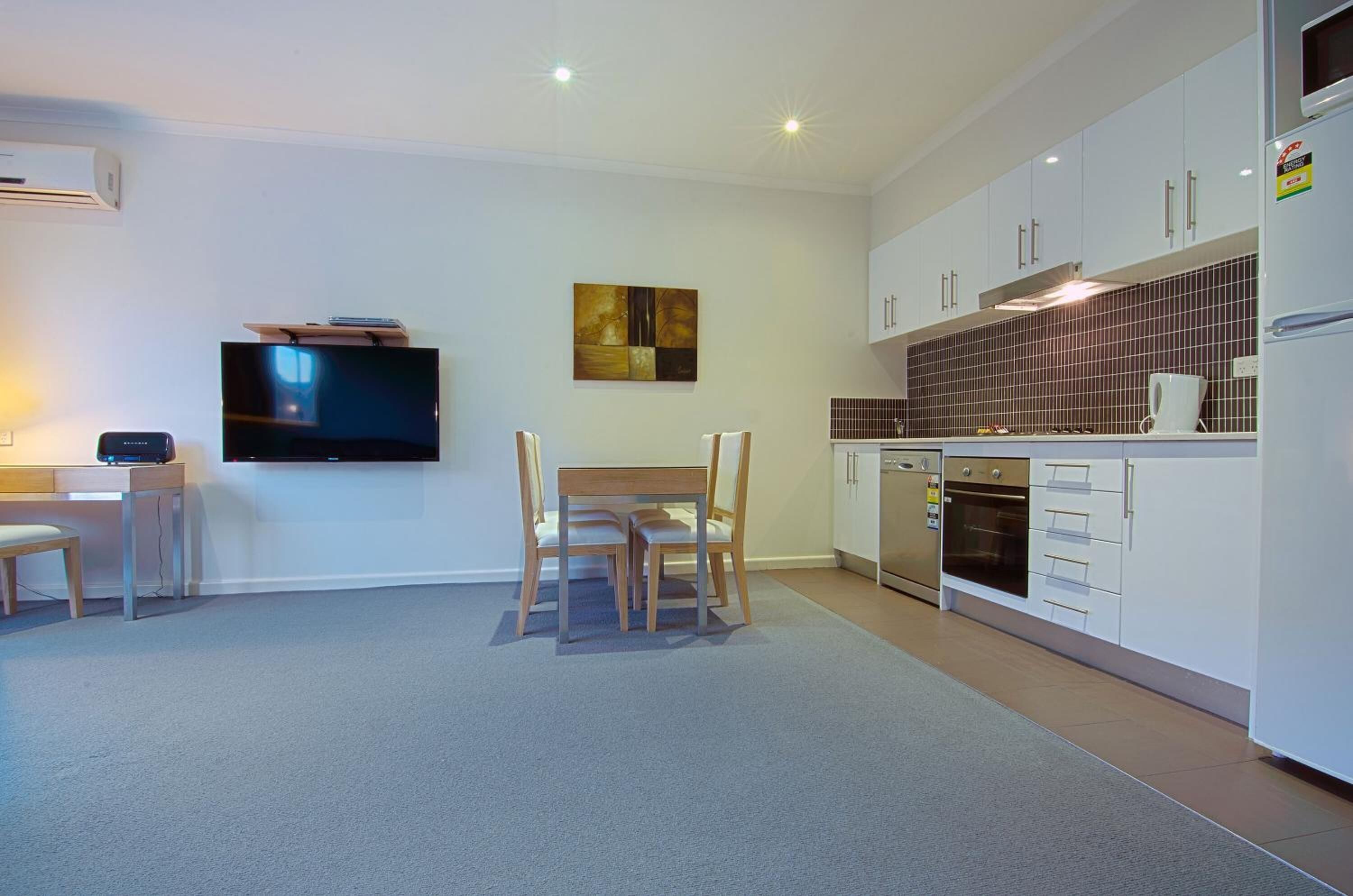 A modern kitchen with white cabinets, a built-in oven, and a flat-screen TV mounted on the wall.