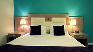 A hotel room with a large bed, two bedside tables with lamps, and a wooden headboard with a letter 'B'. - Brighton Serviced Apartments (Brighton)