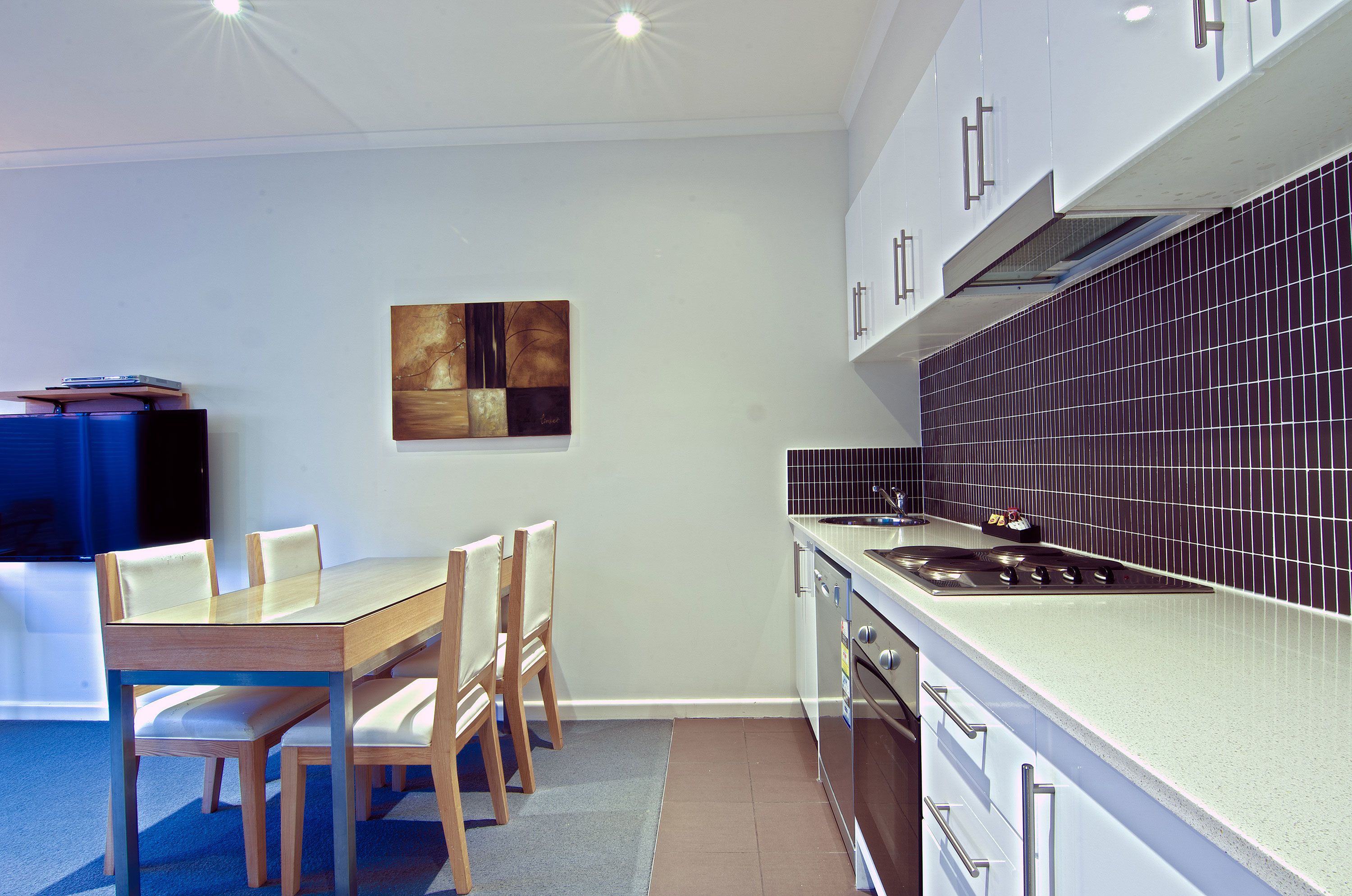 Uma cozinha moderna com área de refeições, destacando uma mesa e cadeiras de madeira, um fogão e um revestimento de azulejos.