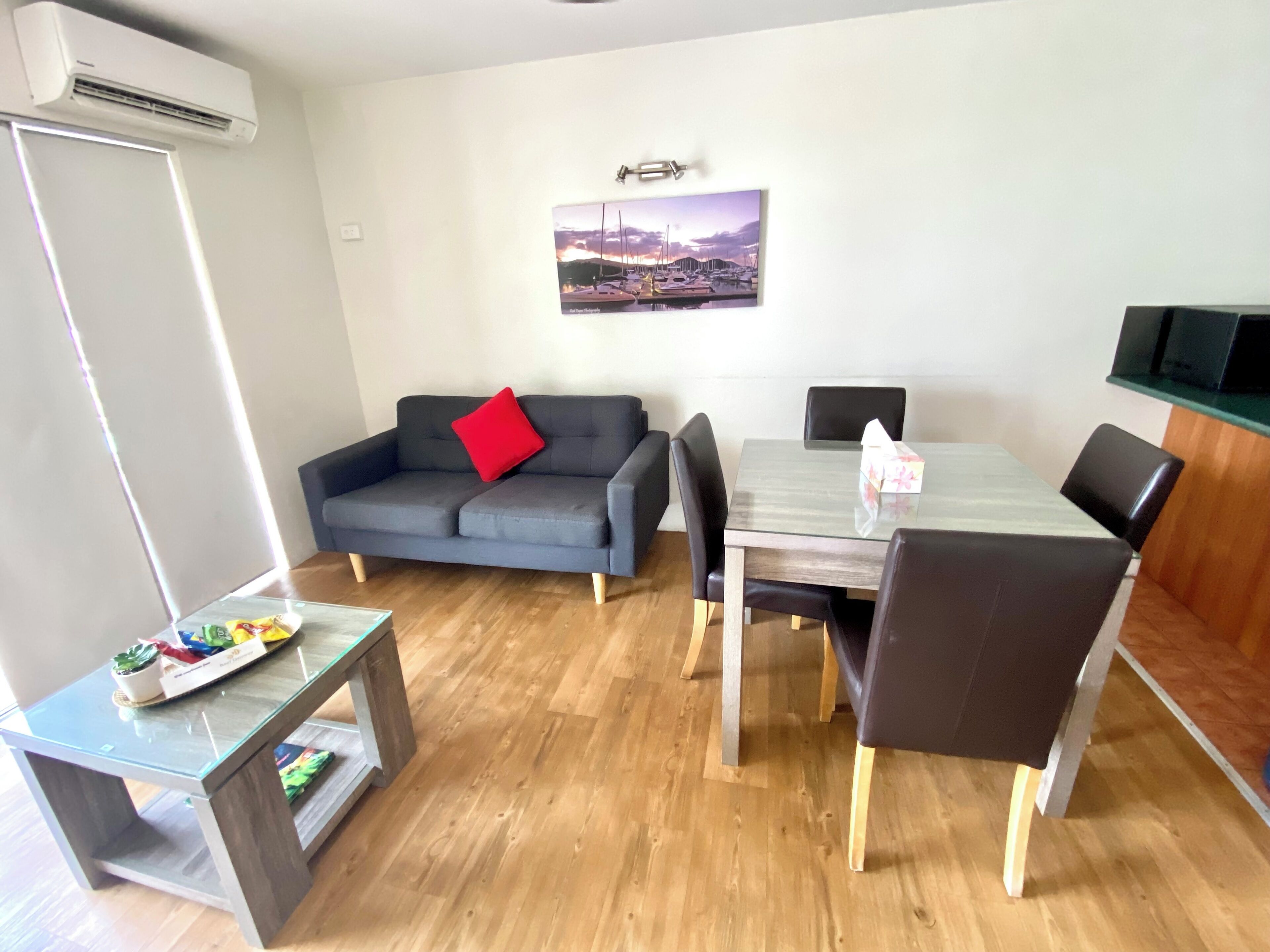A modern living room with a grey sofa, a glass coffee table, and a dining table with chairs.