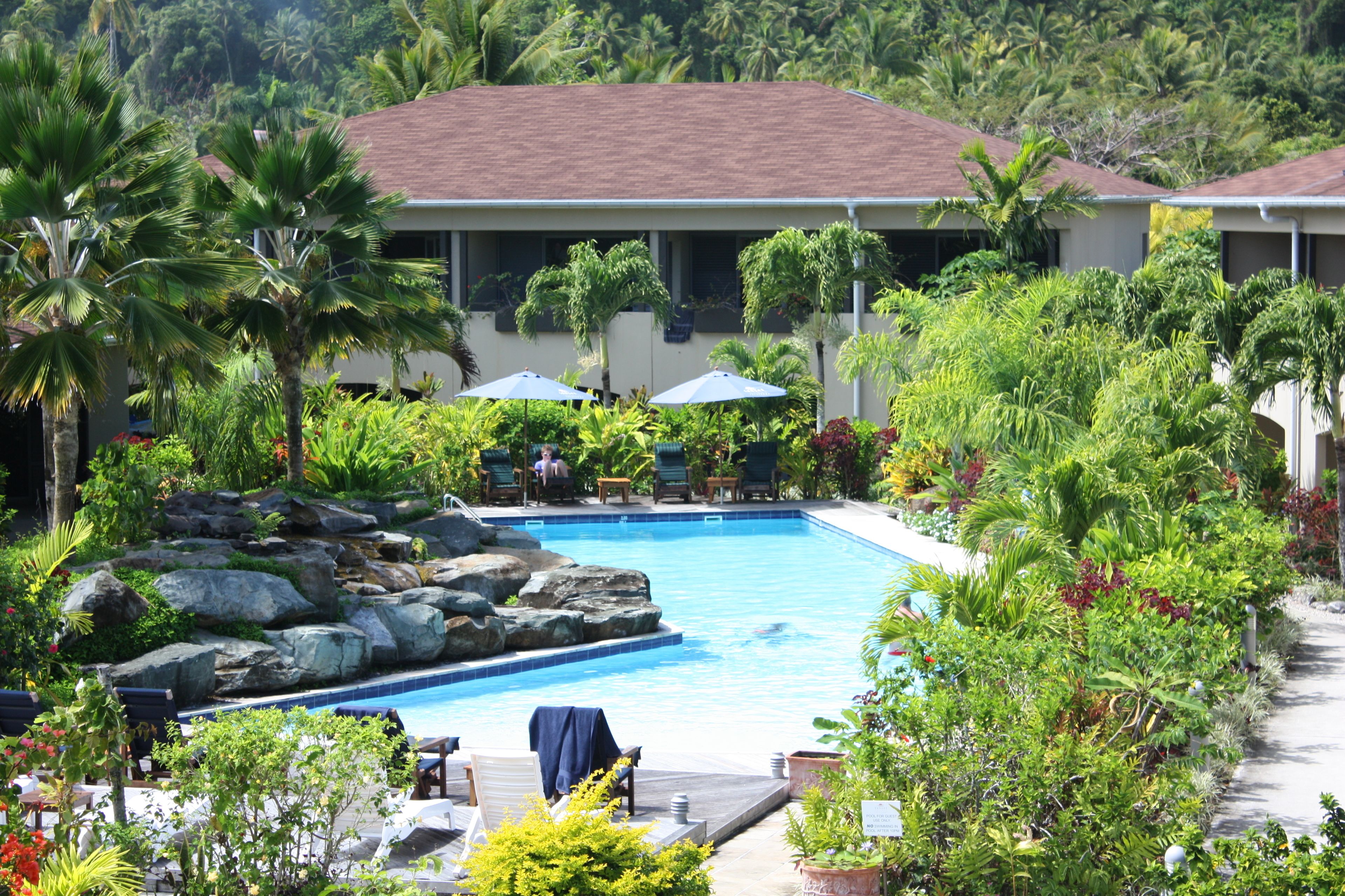 A pool area with lounge chairs, umbrellas, and a building with a red roof.
